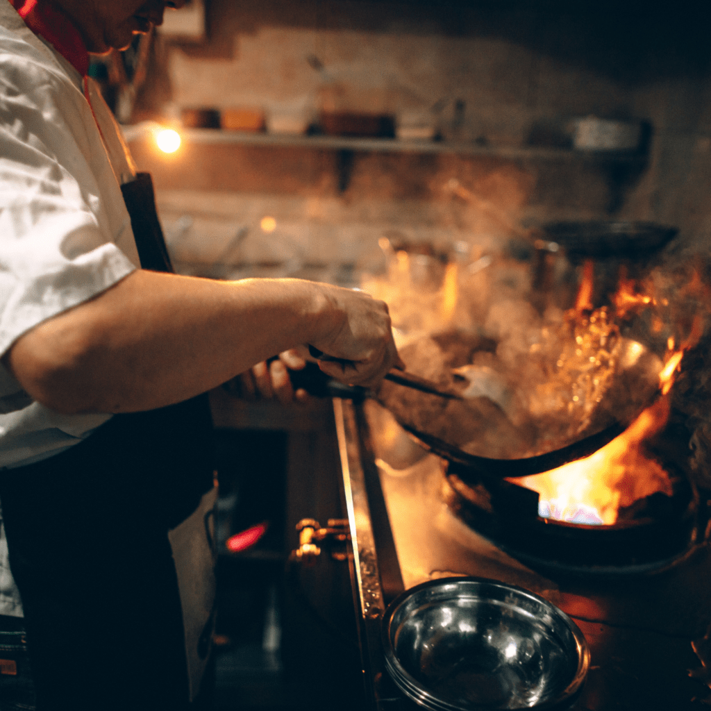 Un chef étoilé dans une cuisine avec un wok et des flammes