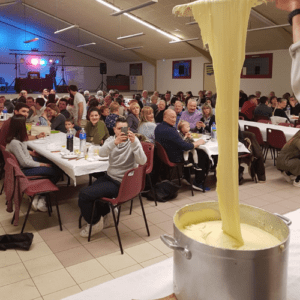 Deux chefs cuisiniers en train de préparer de l'aligot, mélangeant la purée de pommes de terre avec du fromage fondu dans une grande casserole, démontrant leur expertise culinaire.